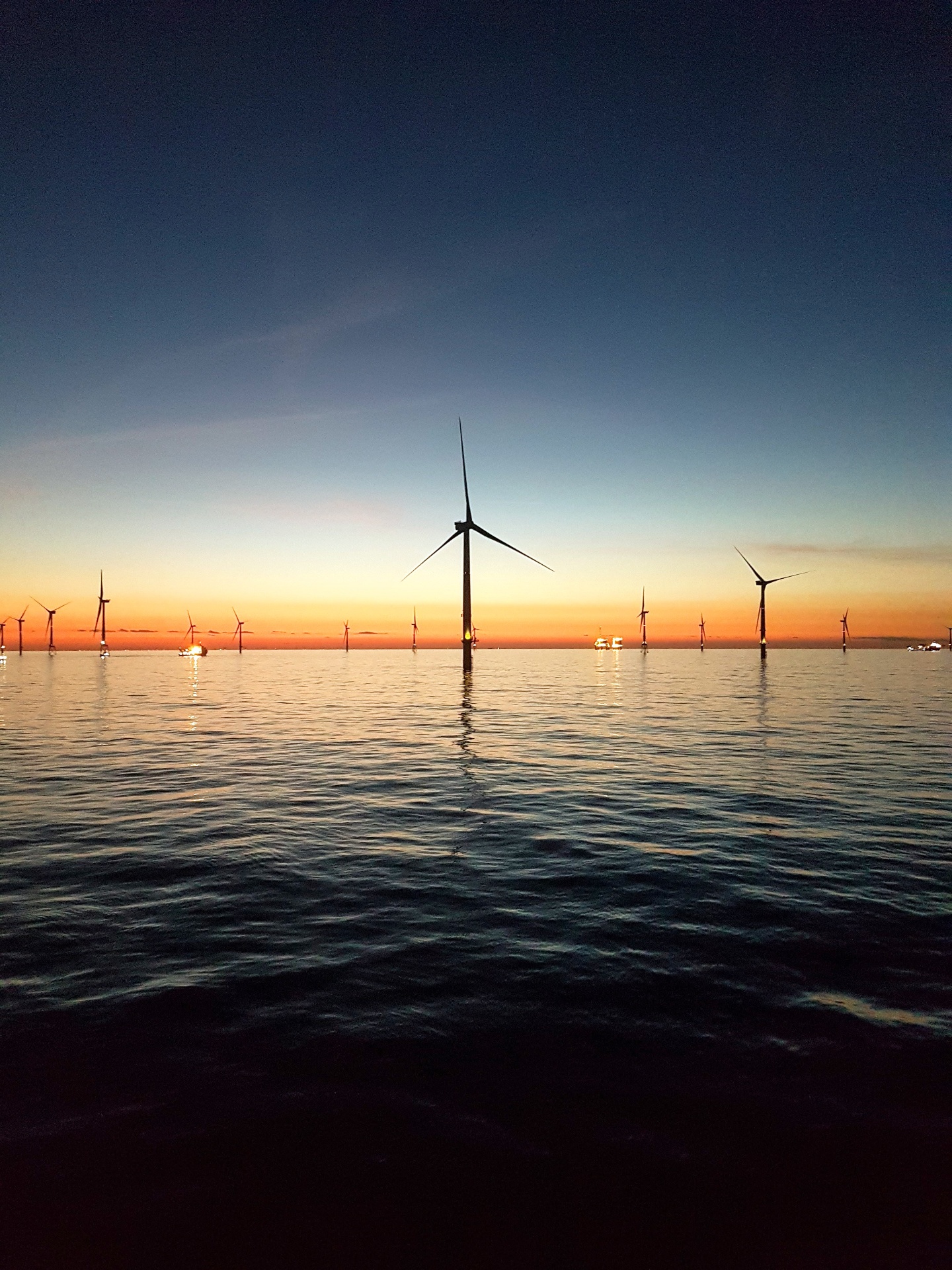 Offshore wind farm at sunset across calm water